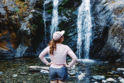 Rear view of woman standing against waterfall