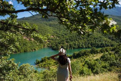 Rear view of woman standing by lake against trees