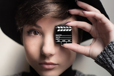 Close-up portrait of young woman covering eye with small film slate