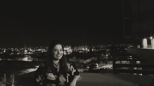 Portrait of smiling young woman in city at night