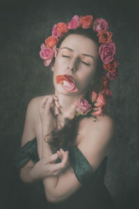 Young female model wearing roses while standing against wall