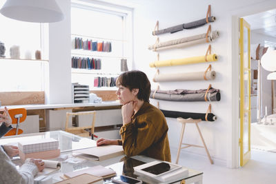 Young female fashion designer in discussion with colleagues in workshop