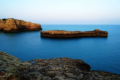 Rock formations by sea against clear sky