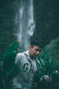 Young man standing against waterfall in forest