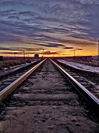 Surface level of railroad tracks against sky at sunset