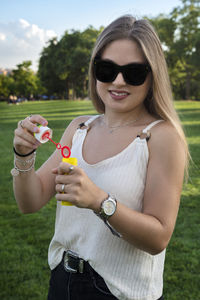 Young woman holding sunglasses while standing outdoors
