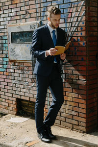 Full length of young man standing against brick wall