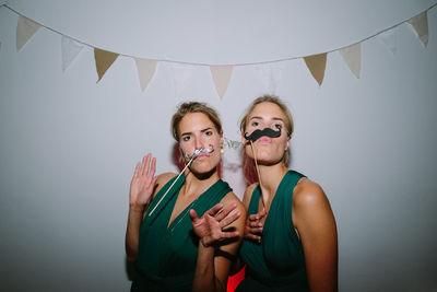 Portrait of twin sisters with mustache props against wall