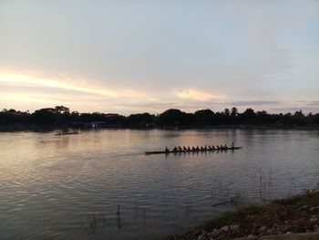 People on lake against sky during sunset