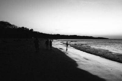 Silhouette people walking on beach against sky