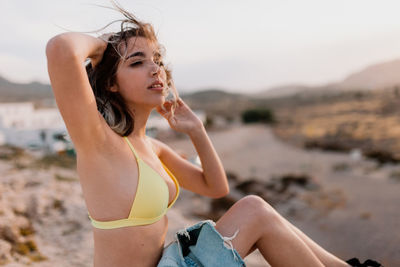 Carefree young woman in yellow bikini on sand at beach
