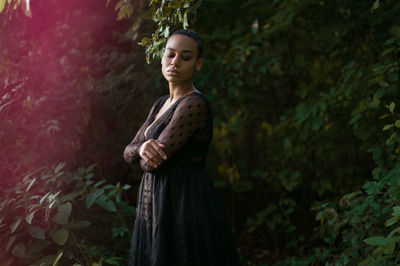 Side view of woman with eyes closed standing against trees in forest