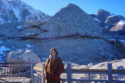 Portrait of young woman standing on snowcapped mountain against clear sky