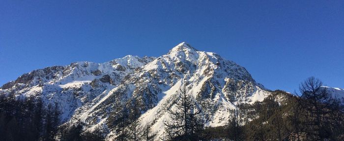 Low angle view of snowcapped mountains against clear blue sky