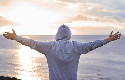 Rear view of man with arms outstretched standing against sea