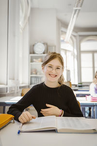 Portrait of happy schoolgirl with book at desk in classroom