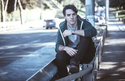 Portrait of young man sitting on street in city