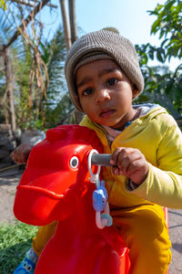 Portrait of cute boy wearing knit hat sitting on toy outdoors
