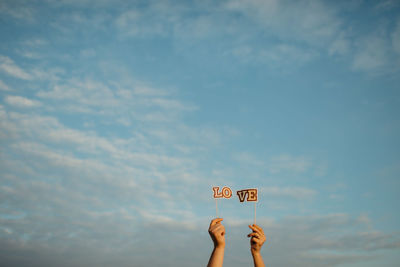 Cropped hands holding love text decor against sky