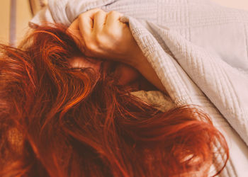 Portrait of woman peeking from blanket at home