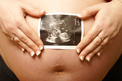 Midsection of pregnant woman holding photograph by abdomen