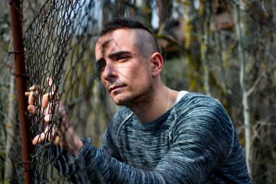 Close-up of thoughtful man looking through chainlink fence