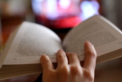 Cropped hand holding book against television set