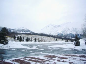 Snowy roads with snow capped mountain and city in background against dreary sky