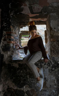 Full length of woman sitting at abandoned building 