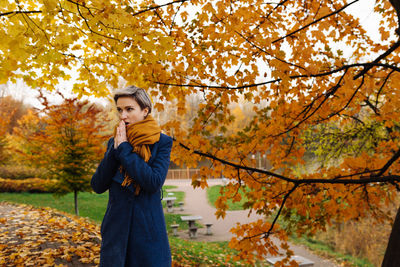 Short-haired woman warms her hands with her breath in the autumn in the park