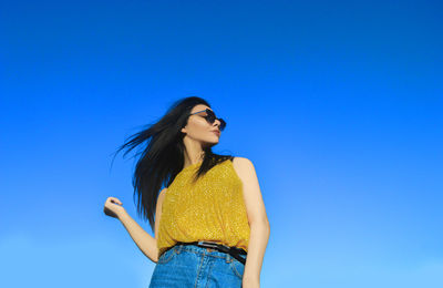 Low angle view of young woman standing against clear blue sky