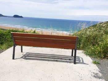 Empty bench on beach by sea against sky