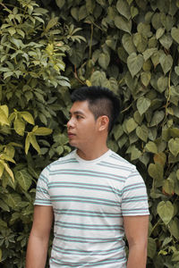 Young man looking away while standing by plants