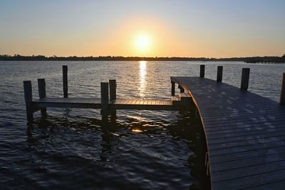 Wooden posts in sea against sky during sunset