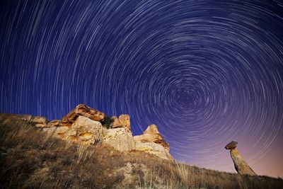 Low angle view of star trail over mountain against sky at night