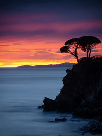 Silhouette rock by sea against romantic sky at sunset