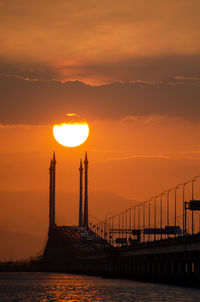 Silhouette bridge over sea against orange sky