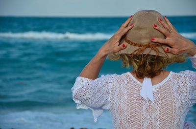 Rear view of woman in hat looking at sea 