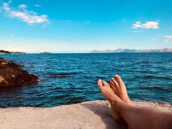 Low section of man wearing shoes while sitting at beach against sky