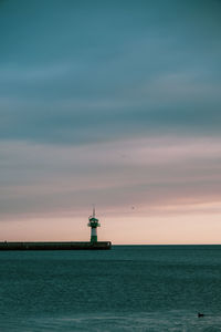 Lighthouse by sea against sky during sunset