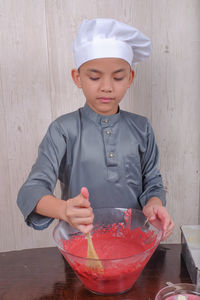 Boy mixing batter in bowl on table at home