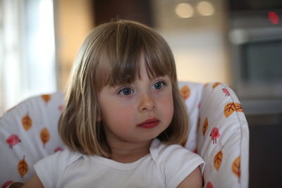 Girl looking away while sitting on high chair at home