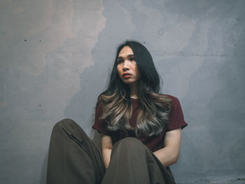 Young woman looking away while sitting on wall