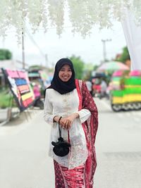 Portrait of smiling young woman standing on street with white kebaya and black pouch