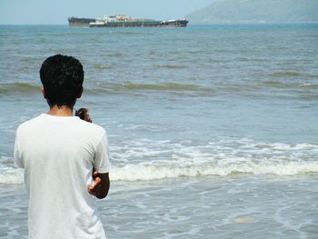 Rear view of young man standing at beach