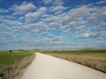 Road passing through field against cloudy sky