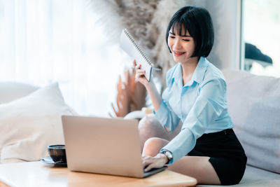 Young woman using laptop while sitting on sofa at home