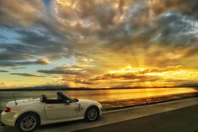 Car on road by sea against sky during sunset