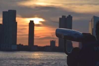 Rear view of people by coin-operated binoculars against orange sky during sunset
