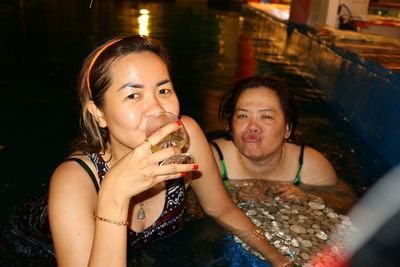 Portrait of woman drinking wine with friend in swimming pool